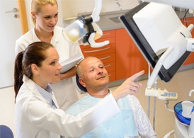 A middle-aged man looking at a screen while his dentist and dental assistant explain what they are looking at