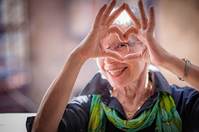 Woman in green scarf smiling and making a heart with her hands