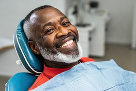 Man in red shirt with white beard smiling in dentist’s chair