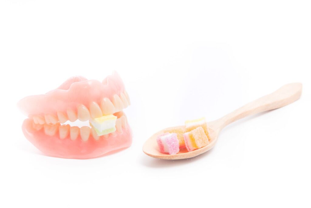 Spoon full of jellies next to a set of dentures biting into one with a white background