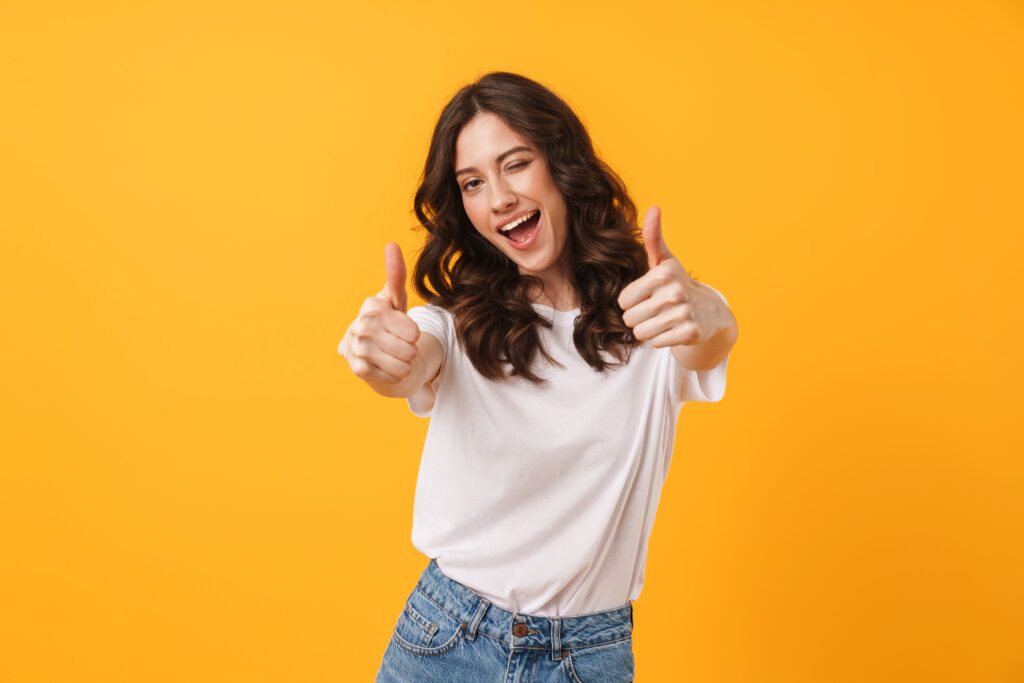 Woman with brown hair smiling, winking, and giving 2 thumbs up